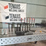 Tenaxis modular welding table setup in a workshop with branded signage and professional clamping tools.