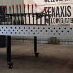 Side perspective of a 1500x3000mm ESS raw cast iron welding table on a standard round fixed leg with caster wheel