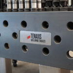 Close-up of the Tenaxis logo on the side of a 1500x3000mm nitrided cast iron welding table.