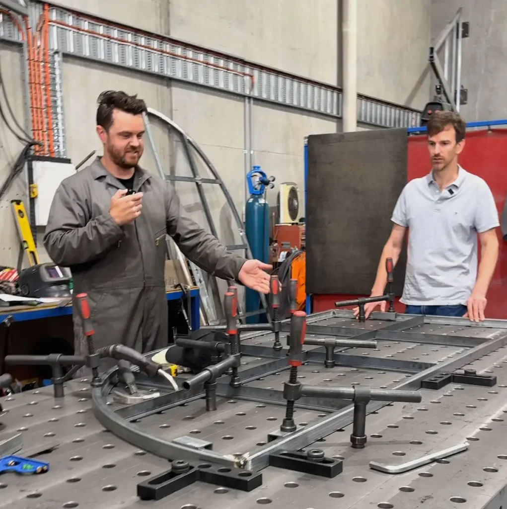 Tenaxis founder Ray and Nick from UrbanxSteel demonstrating industrial workholding techniques on a modular 3D welding table using heavy-duty screw clamps and precision squaring tools.