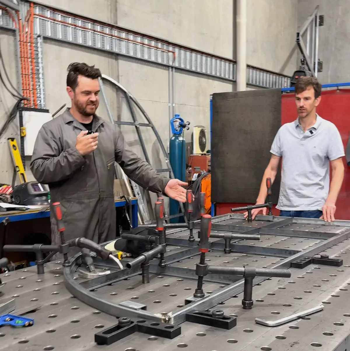 Tenaxis founder Ray and Nick from UrbanxSteel demonstrating industrial workholding techniques on a modular 3D welding table using heavy-duty screw clamps and precision squaring tools.