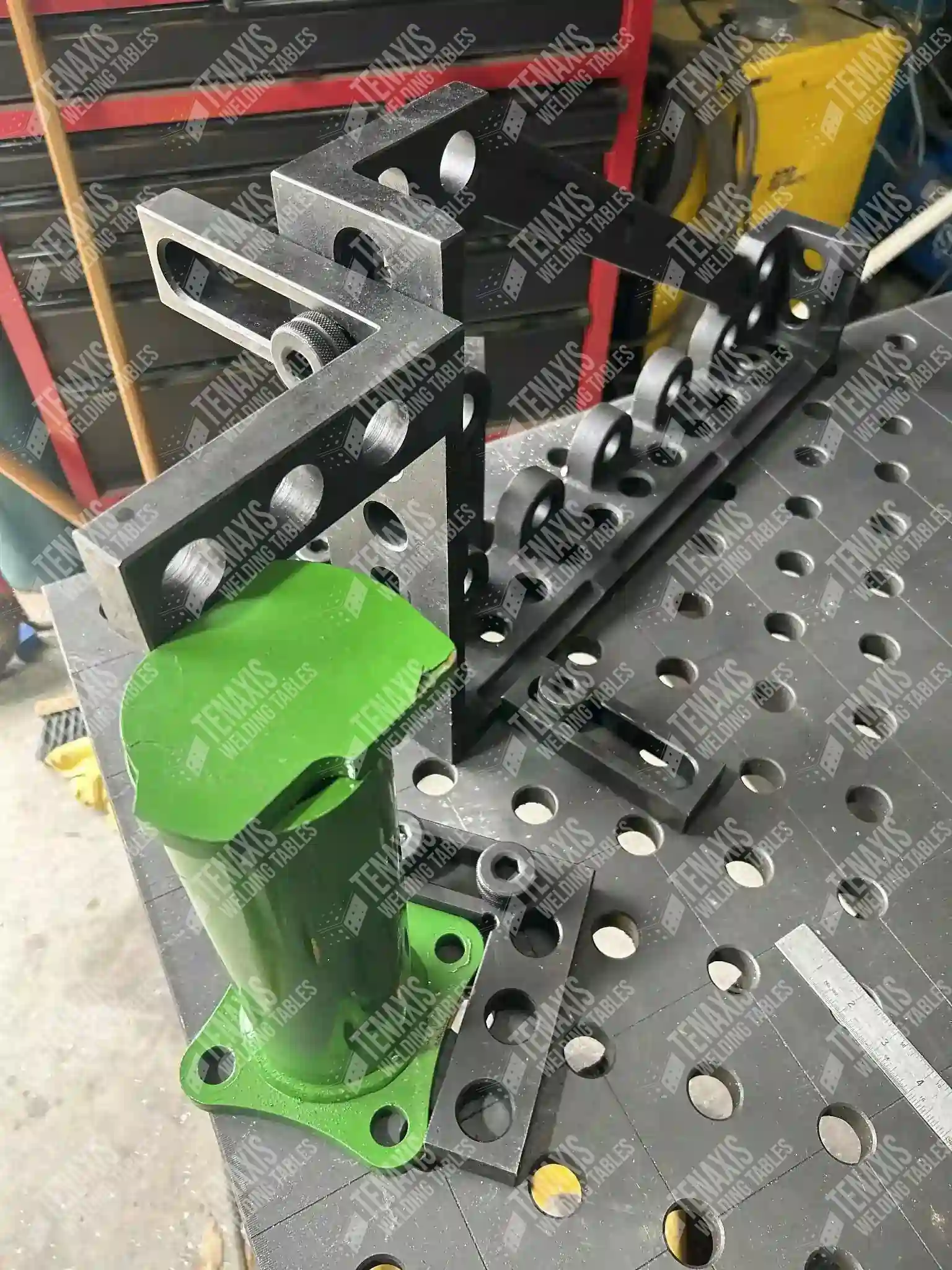 Close-up of a green specialized pipe support fixture mounted on a 28mm diagonal hole pattern precision welding fixture table.
