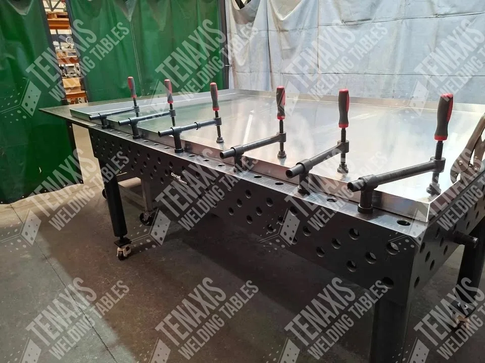 A heavy-duty steel sheet being clamped flat for precision welding using a Tenaxis modular welding table.